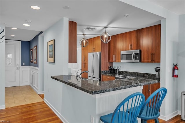 kitchen with stainless steel appliances, visible vents, brown cabinetry, dark stone countertops, and a peninsula