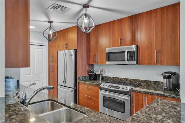 kitchen with visible vents, appliances with stainless steel finishes, brown cabinets, dark stone countertops, and a sink