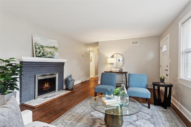 living room with a brick fireplace, visible vents, baseboards, and wood finished floors