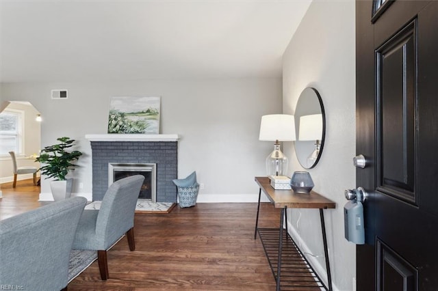 foyer featuring baseboards, visible vents, arched walkways, dark wood-style floors, and a brick fireplace