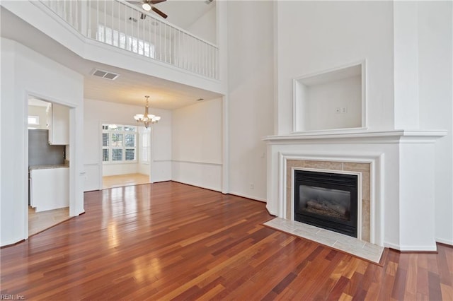 unfurnished living room with ceiling fan with notable chandelier, a fireplace, wood finished floors, a towering ceiling, and visible vents