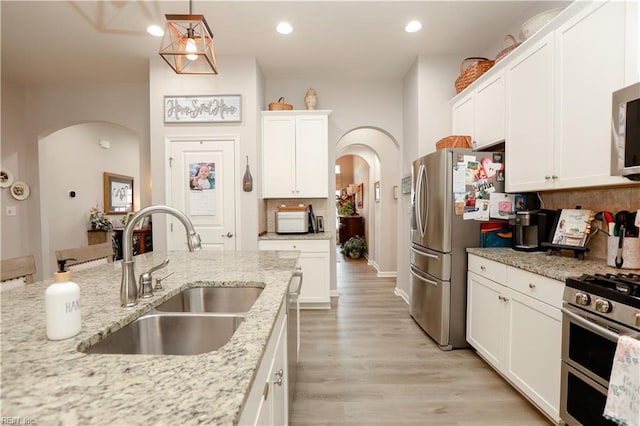 kitchen with tasteful backsplash, stainless steel appliances, arched walkways, white cabinetry, and a sink