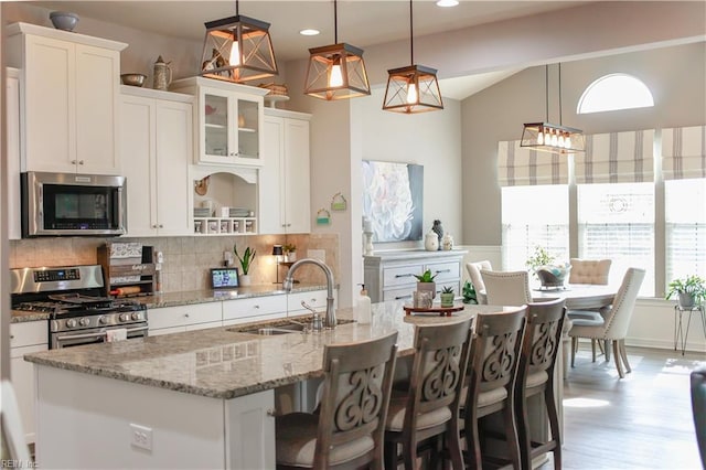 kitchen featuring a kitchen island with sink, a sink, tasteful backsplash, appliances with stainless steel finishes, and white cabinets