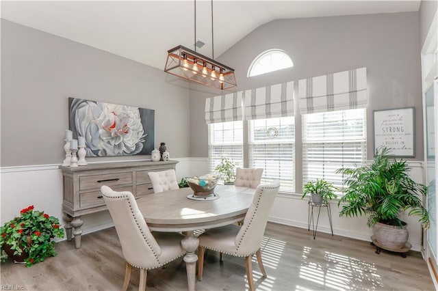 dining area with lofted ceiling, a wainscoted wall, and light wood finished floors