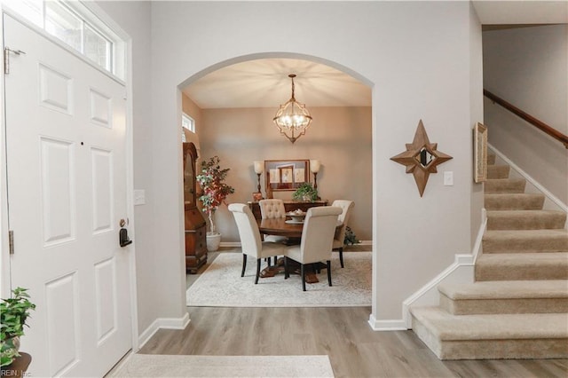 entryway featuring arched walkways, an inviting chandelier, stairs, and light wood finished floors