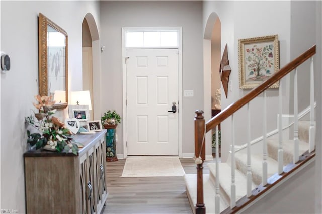 foyer with baseboards, arched walkways, wood finished floors, and stairs