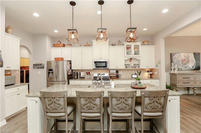 kitchen with a sink, a spacious island, stainless steel appliances, arched walkways, and decorative backsplash