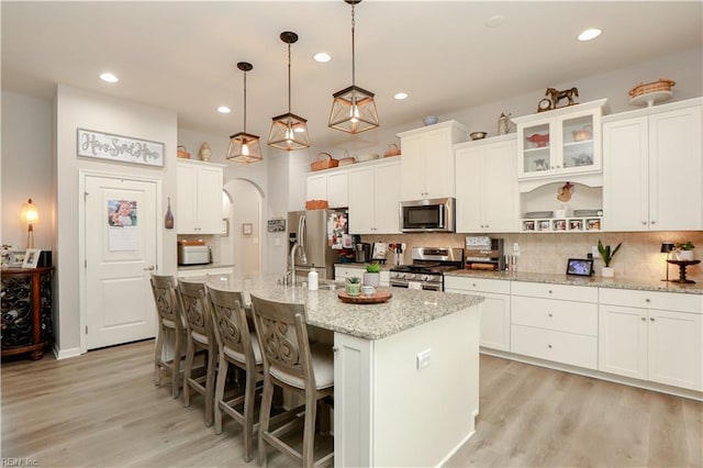 kitchen featuring arched walkways, backsplash, appliances with stainless steel finishes, and light wood-style flooring