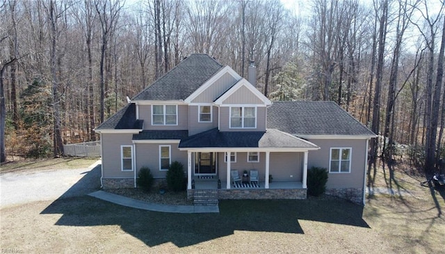 view of front of home featuring covered porch, a shingled roof, a front lawn, and a view of trees