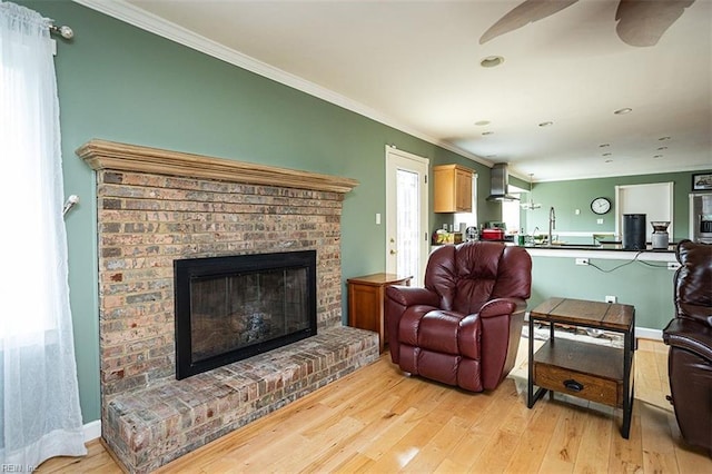 living room with a fireplace, crown molding, light wood-style flooring, and baseboards