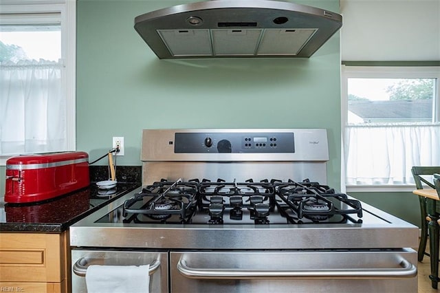 kitchen with a healthy amount of sunlight, stainless steel gas range, extractor fan, and dark stone countertops