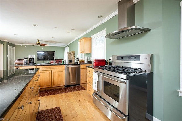 kitchen with light wood finished floors, a ceiling fan, wall chimney exhaust hood, stainless steel appliances, and crown molding