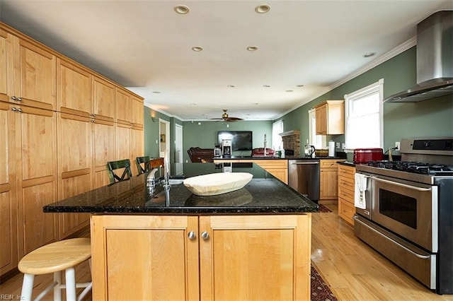 kitchen with a center island, light wood finished floors, appliances with stainless steel finishes, dark stone counters, and wall chimney exhaust hood