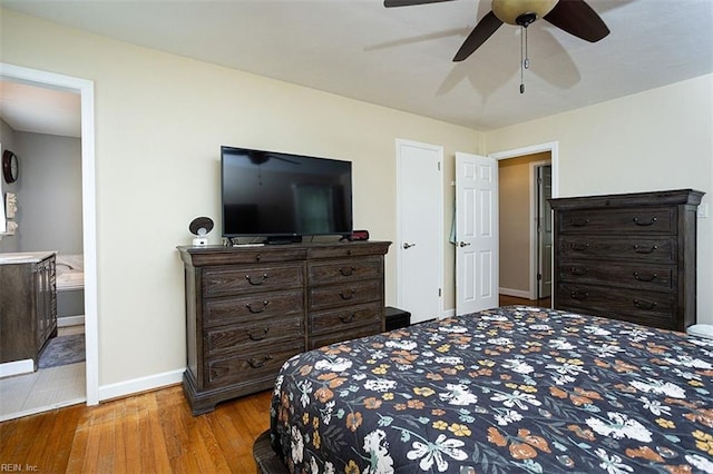 bedroom featuring ceiling fan, baseboards, wood finished floors, and ensuite bathroom