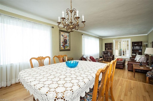 dining area featuring crown molding, french doors, a chandelier, and light wood-style floors