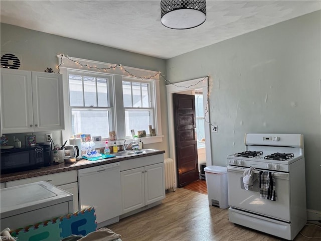 kitchen featuring light wood finished floors, radiator heating unit, white cabinets, a sink, and white appliances