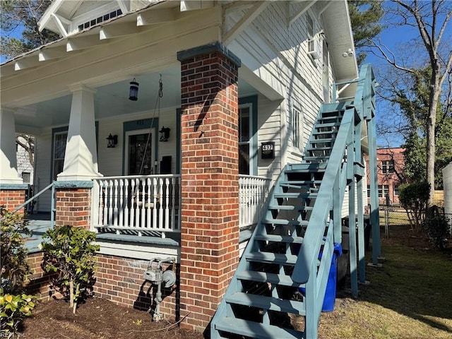 view of property exterior with stairs, brick siding, and covered porch