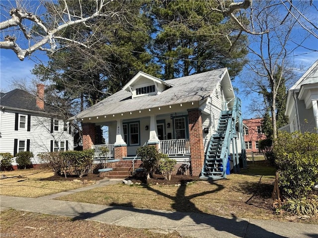 view of front of property with covered porch, brick siding, and stairway