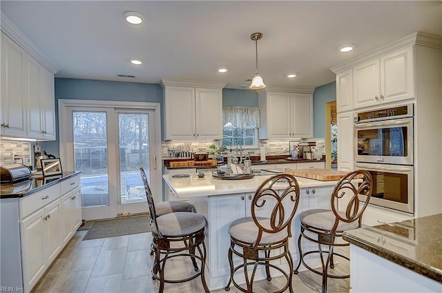 kitchen featuring stainless steel double oven, white cabinetry, visible vents, and a kitchen bar