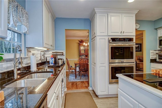 kitchen with white cabinets, light wood-style flooring, appliances with stainless steel finishes, a sink, and backsplash