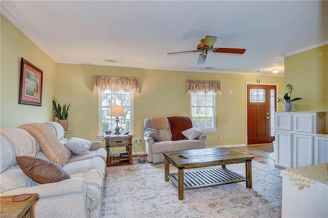 living area with baseboards, visible vents, ceiling fan, and crown molding