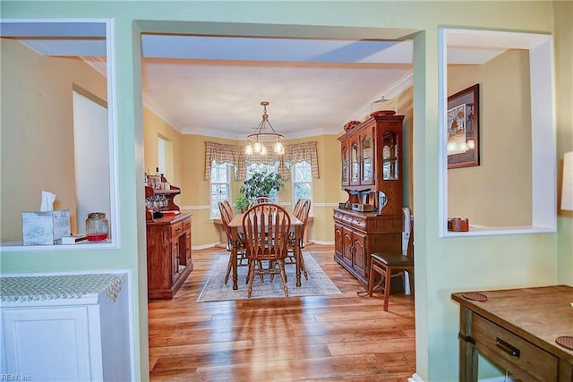 dining area featuring ornamental molding, light wood-type flooring, and an inviting chandelier