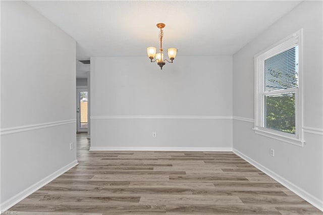 unfurnished room featuring wood finished floors, baseboards, and an inviting chandelier