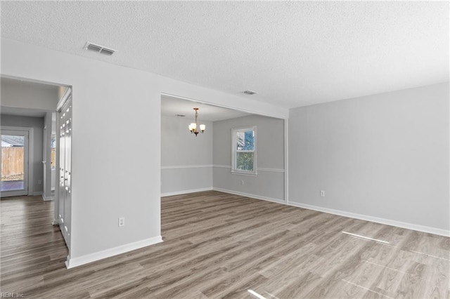 spare room with a textured ceiling, a notable chandelier, wood finished floors, visible vents, and baseboards