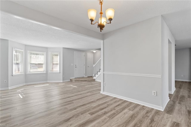 unfurnished living room featuring stairs, a textured ceiling, wood finished floors, and a chandelier