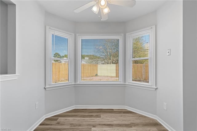 spare room featuring baseboards, ceiling fan, wood finished floors, and a healthy amount of sunlight