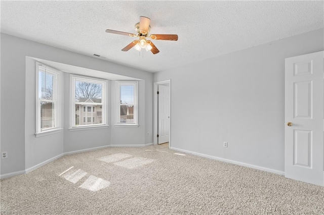 empty room with visible vents, light colored carpet, ceiling fan, a textured ceiling, and baseboards