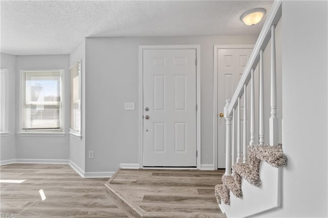 foyer entrance featuring baseboards, a textured ceiling, stairs, and light wood-style floors