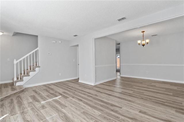 unfurnished living room featuring a chandelier, wood finished floors, a textured ceiling, and stairs