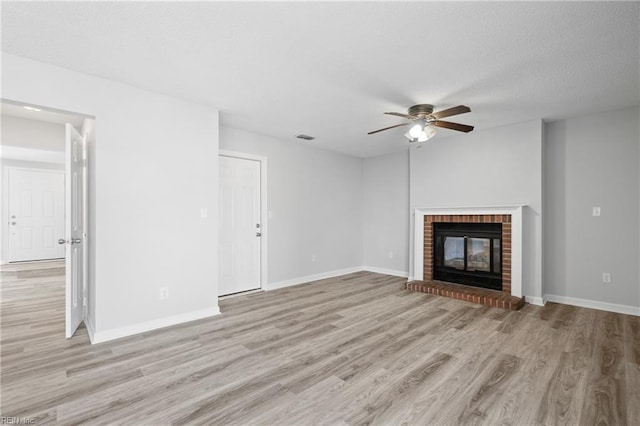 unfurnished living room with light wood finished floors, visible vents, a brick fireplace, a textured ceiling, and baseboards