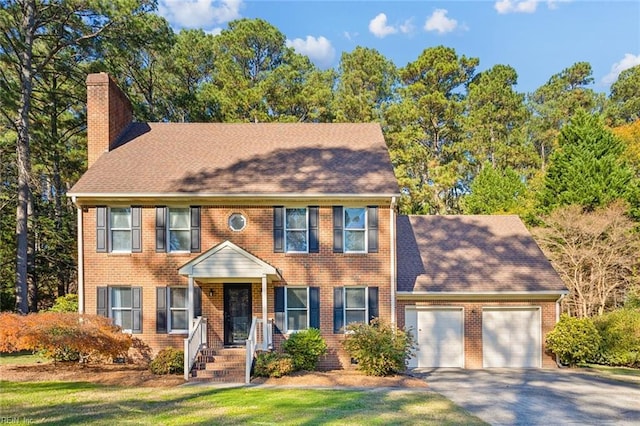 colonial-style house featuring aphalt driveway, a chimney, an attached garage, and brick siding