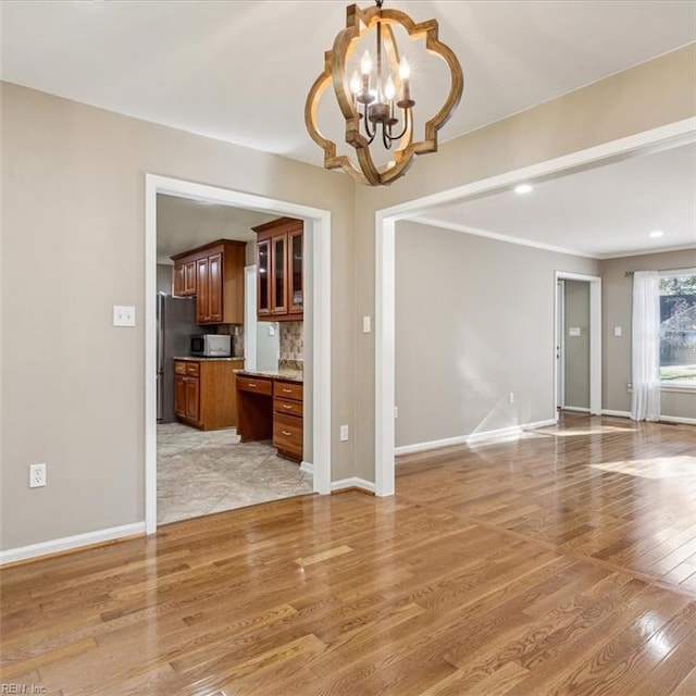 unfurnished living room with a chandelier, baseboards, and light wood finished floors