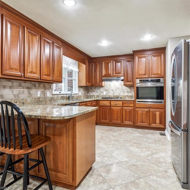 kitchen featuring appliances with stainless steel finishes, under cabinet range hood, brown cabinets, and a peninsula