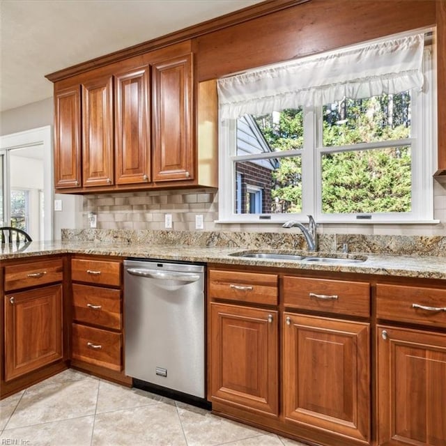 kitchen with plenty of natural light, brown cabinetry, light stone countertops, stainless steel dishwasher, and a sink