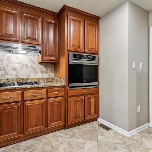 kitchen featuring under cabinet range hood, visible vents, appliances with stainless steel finishes, brown cabinets, and tasteful backsplash