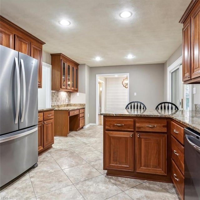 kitchen featuring appliances with stainless steel finishes, brown cabinets, a peninsula, light stone countertops, and built in desk