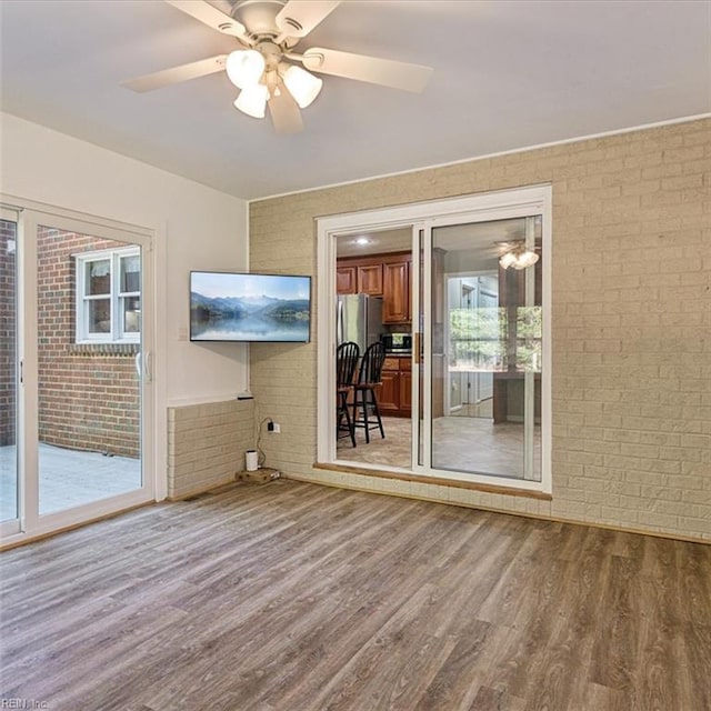 unfurnished room featuring brick wall, wood finished floors, and a ceiling fan