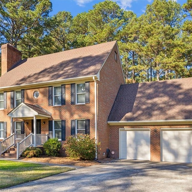 colonial home with a garage, driveway, a chimney, and brick siding