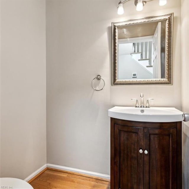 half bath featuring toilet, baseboards, wood finished floors, and vanity