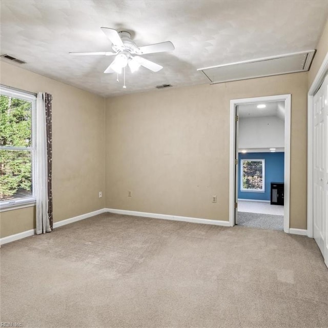 carpeted empty room featuring attic access, visible vents, ceiling fan, and baseboards