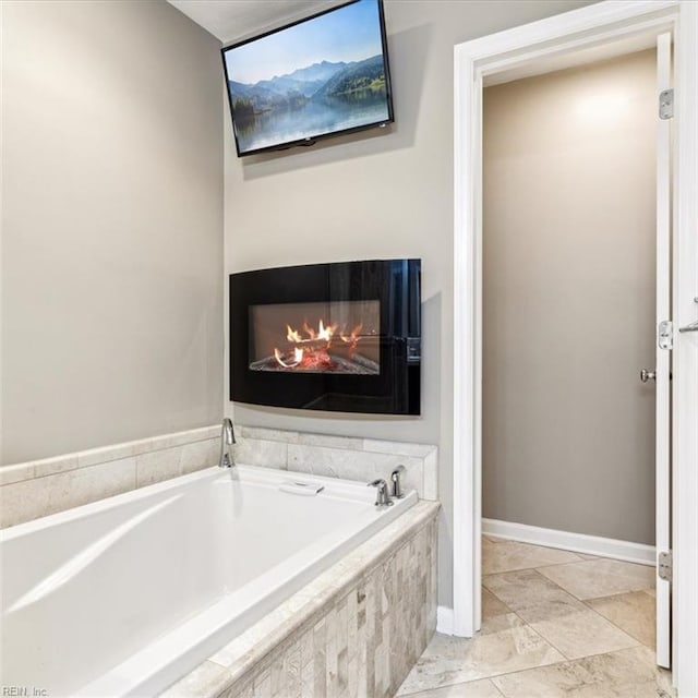 full bath with a warm lit fireplace, a garden tub, and baseboards