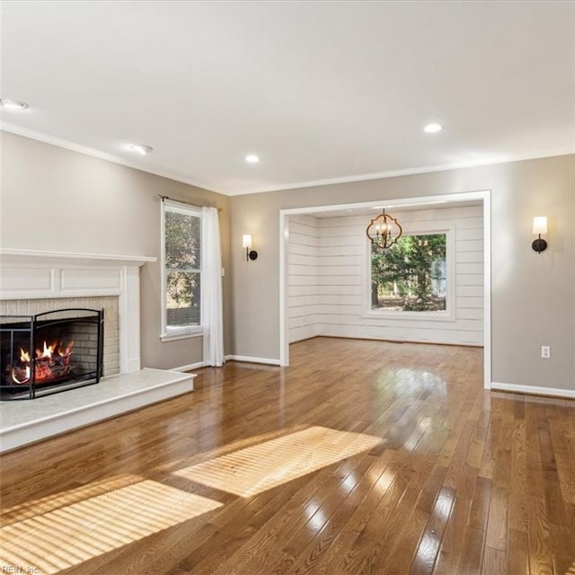 unfurnished living room with a brick fireplace, wood-type flooring, baseboards, and ornamental molding