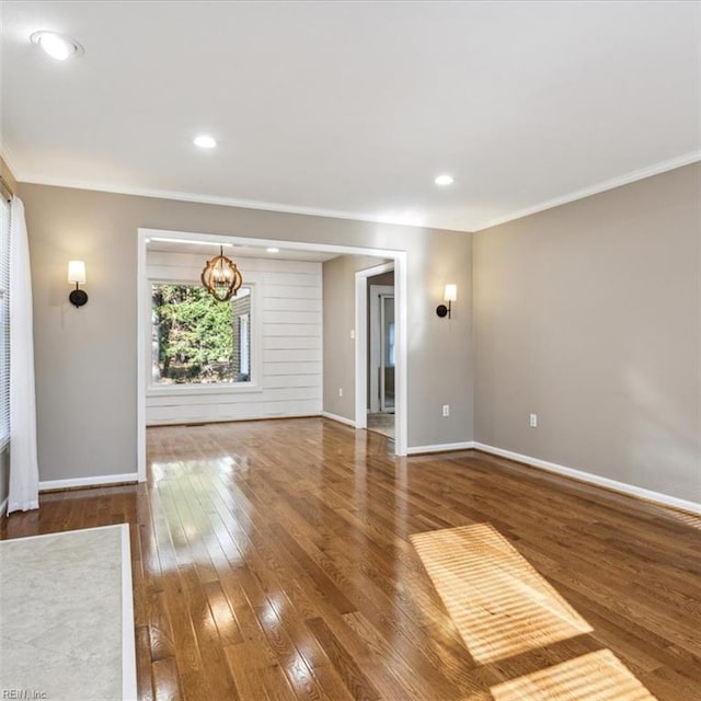 unfurnished room with baseboards, wood-type flooring, ornamental molding, an inviting chandelier, and recessed lighting