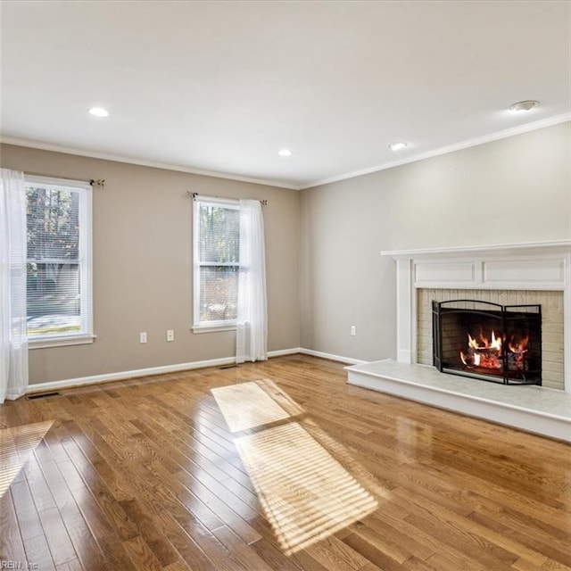 unfurnished living room with a brick fireplace, baseboards, ornamental molding, and hardwood / wood-style floors