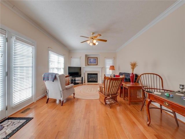 interior space with light wood finished floors, visible vents, a glass covered fireplace, ceiling fan, and crown molding