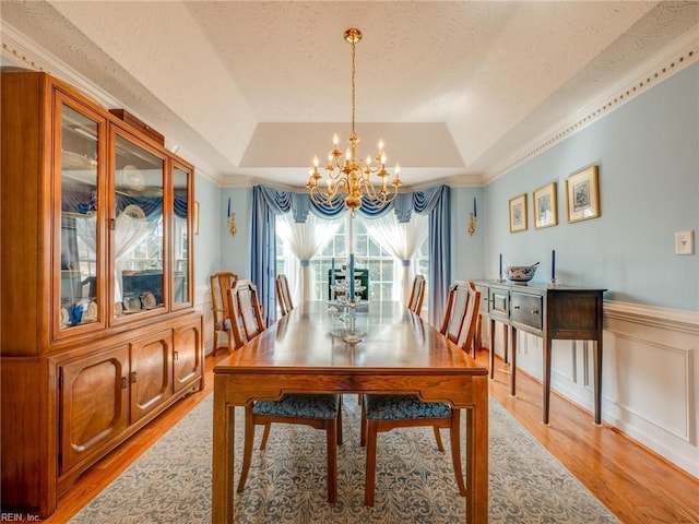 dining space with a textured ceiling, a wainscoted wall, light wood-type flooring, a tray ceiling, and an inviting chandelier